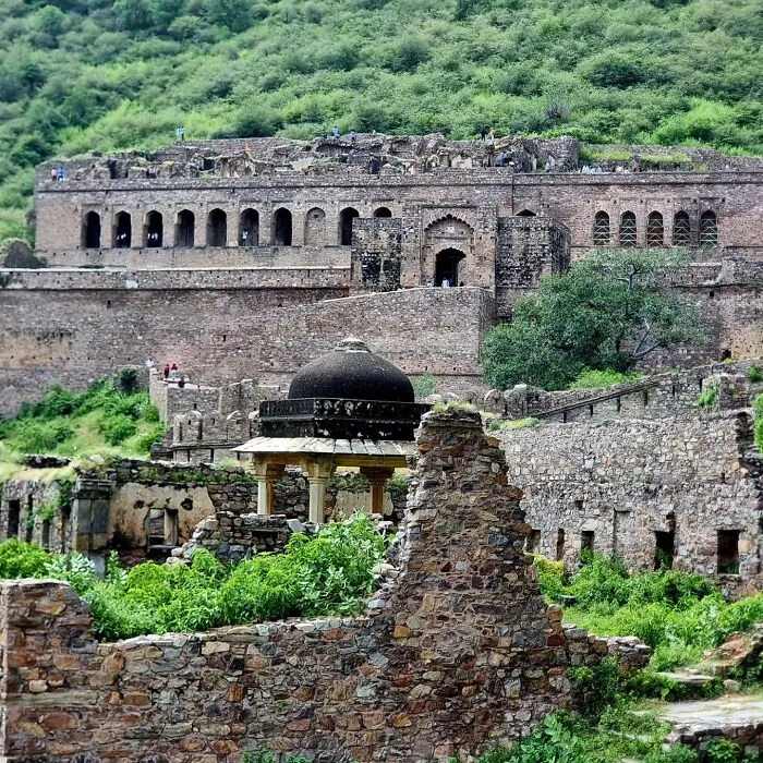 Ancient abandoned places with stone ruins overgrown with greenery set against a forested hillside background.