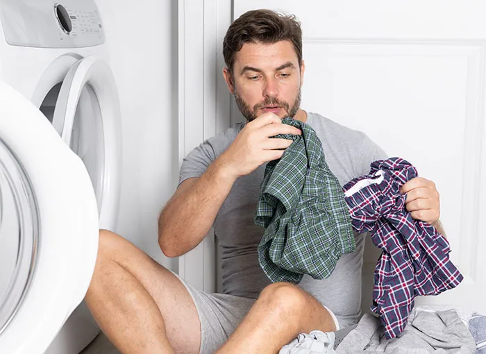 Man sitting by washing machine smelling clothes, illustrating bizarre reasons why someone wanted a divorce concept.