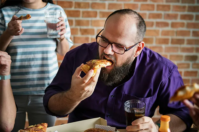 Man with beard and glasses eating pizza, holding a drink, illustrating bizarre reasons why someone wanted divorce.