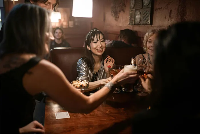 Group of friends clinking glasses in a dimly lit bar, smiling and enjoying a casual night out, divorce reasons theme.