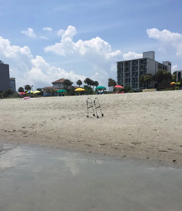 Andador en la arena de la playa con sombrillas coloridas y edificios al fondo en vacaciones de verano.