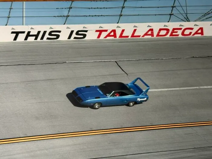 Blue Plymouth muscle car racing on Talladega track, featured in a popular online thread of exciting car pics.