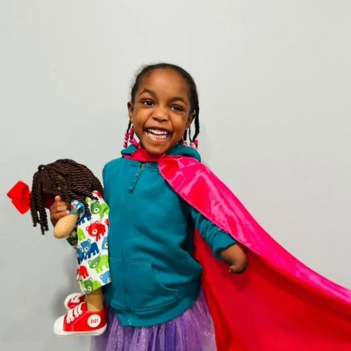 Young girl with a rare health condition smiling and holding a custom doll representing her needs and uniqueness.