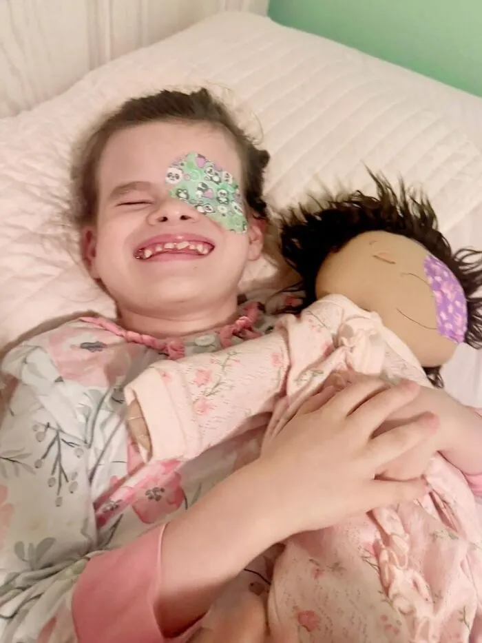 Smiling child with a patch over one eye holding a doll designed to represent rare health conditions and individual needs