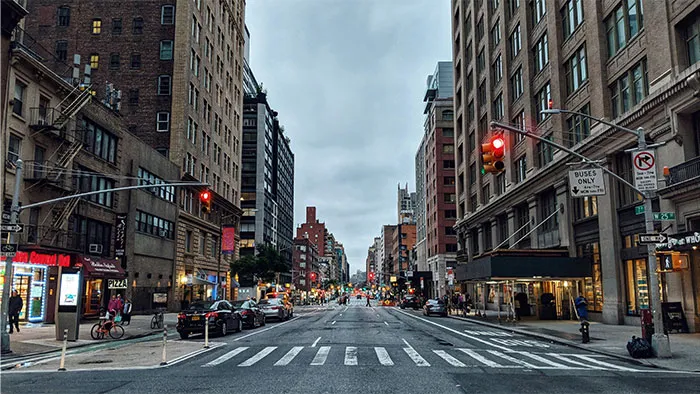 City street scene near the Boston Marathon route with buildings, traffic lights, and pedestrians under a cloudy sky.