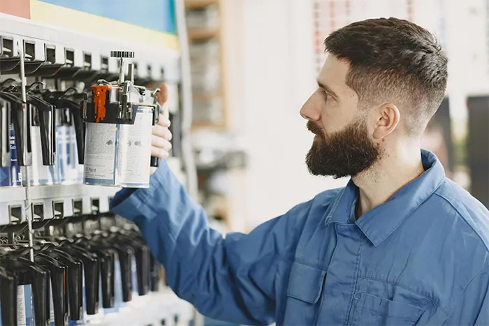 Man in blue coveralls selecting a paint can from a shelf in a workshop, focusing on his task carefully.
