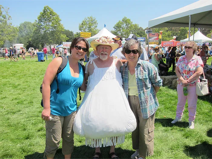 Three people smiling at an outdoor event during the Boston Marathon, enjoying a sunny day with tents in the background.