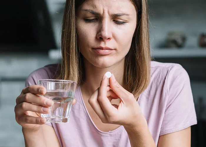 Young woman holding a pill and glass of water, concerned about illness after doctors got diagnosis wrong.