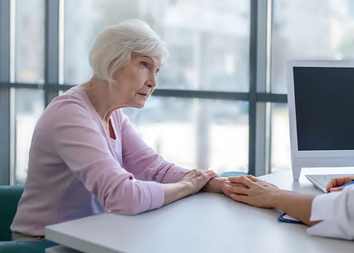 Elderly woman consulting doctor, showing concern about misdiagnosis and serious illness despite being too young to be sick.