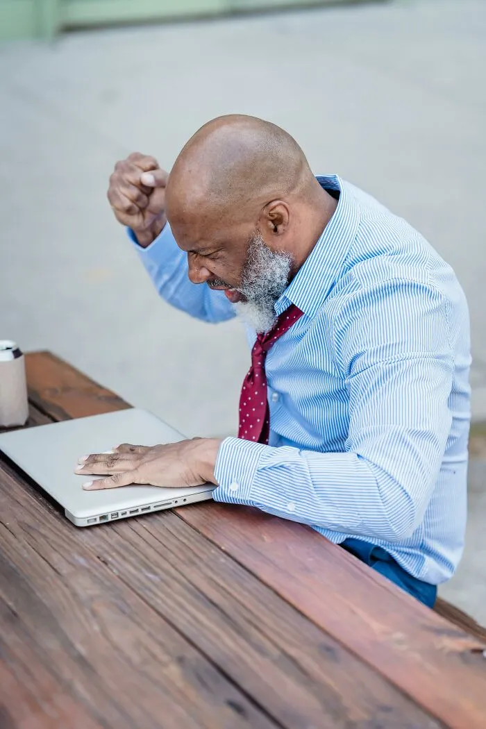 Frustrated man in a blue shirt and red tie angrily closing laptop, representing bosses being out of touch at work.