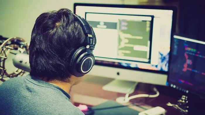 Person wearing headphones working on coding at a dual monitor setup, illustrating frustratingly out of touch bosses scenario.