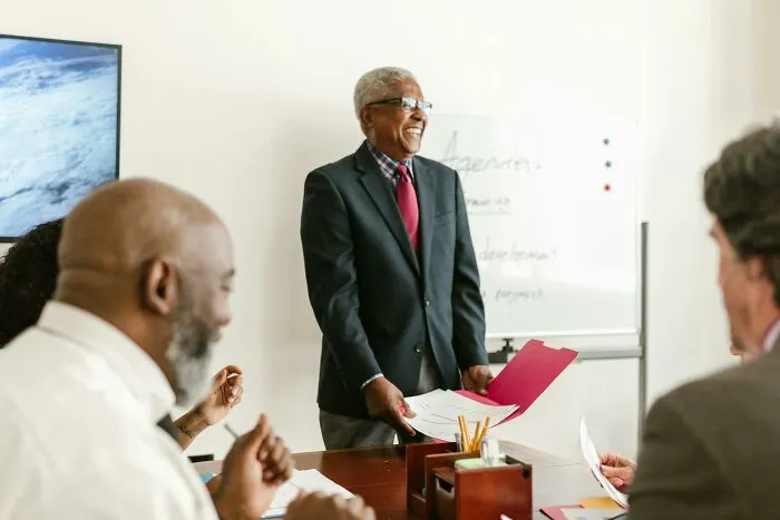 Older male boss in a suit leading a meeting with colleagues, illustrating frustratingly out of touch bosses in an office setting.