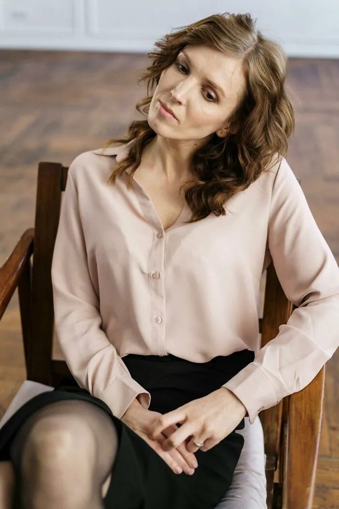 Woman in thoughtful pose sitting on wooden chair, reflecting on signs of talking to a psychopath in a calm setting.