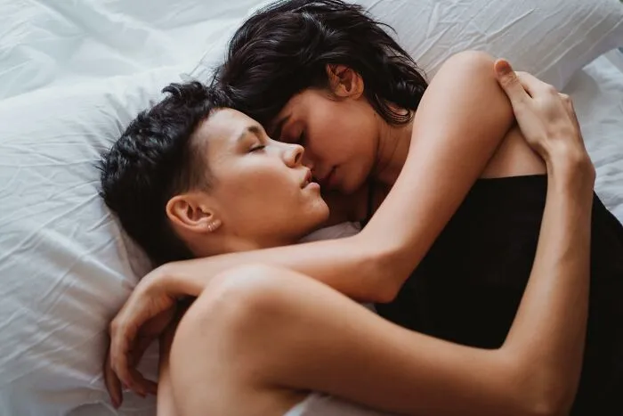 Two people lying closely together on a bed, conveying intimacy and hidden family secrets discovered after someone passed.