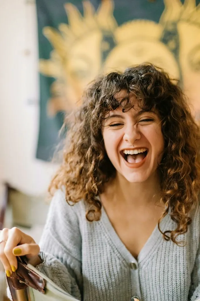 Young woman with curly hair laughing joyfully in a cozy room, capturing moments of talking to a psychopath.