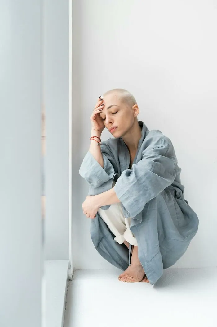 Young person in a blue robe sitting by a window looking distressed, reflecting on talking to a psychopath experiences.