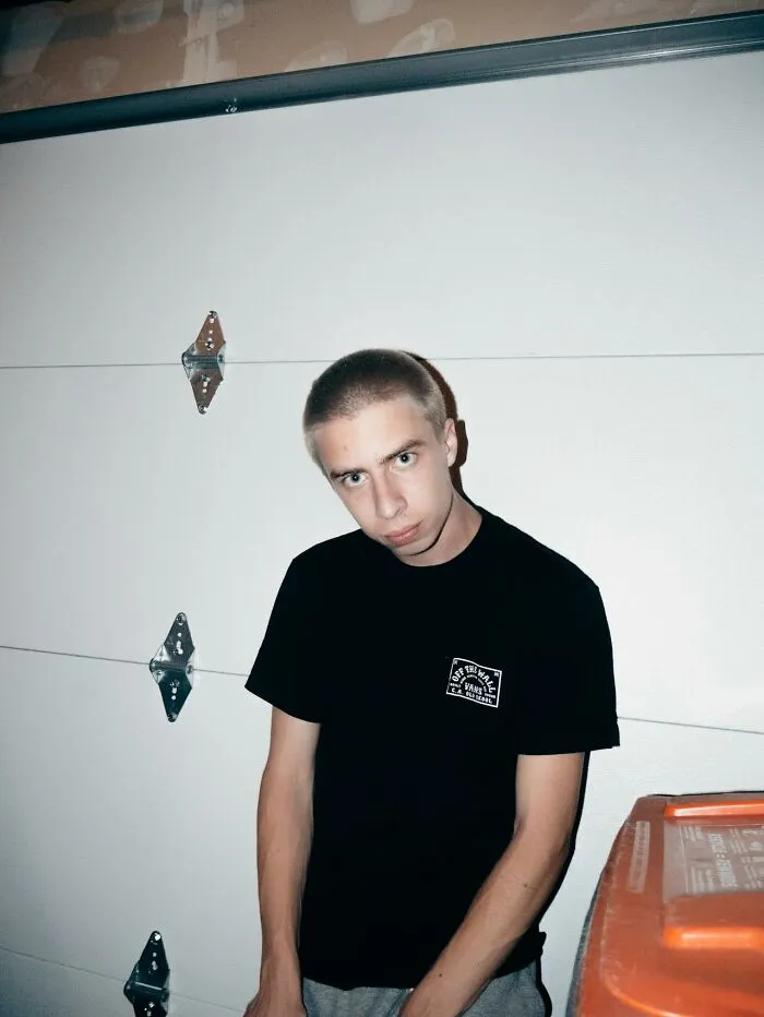 Young man with intense gaze leaning against a garage door, illustrating behavior linked to talking to a psychopath.