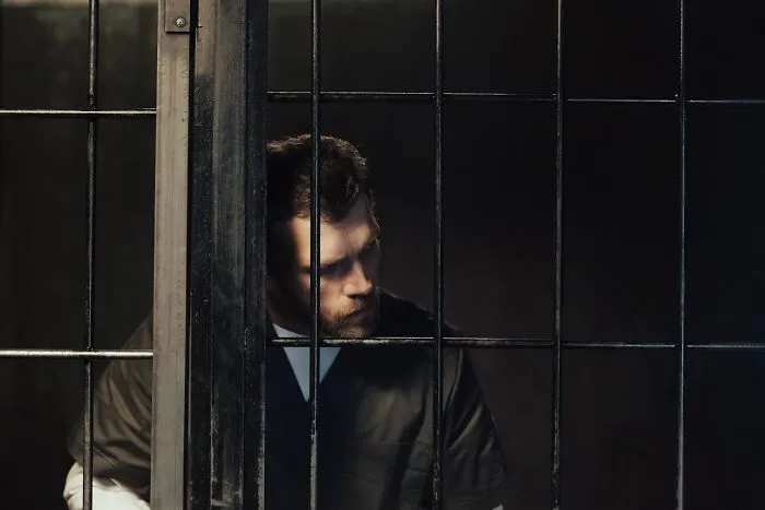 Man behind prison bars looking down, illustrating the concept of talking to a psychopath and recognizing warning signs.