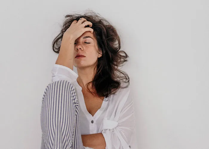 Woman sitting against a white wall, looking distressed and overwhelmed, illustrating real-life terror and paranoia.