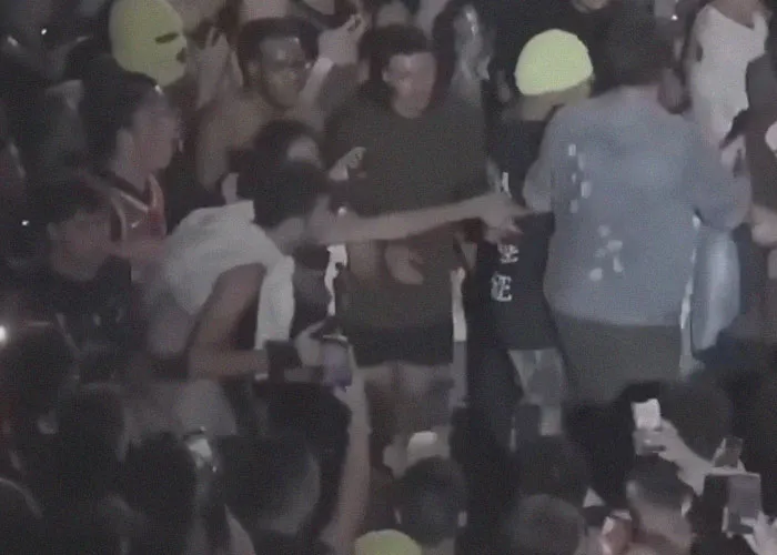 Crowd at night with people facing real-life terror, capturing moments with phones and reacting in disbelief.