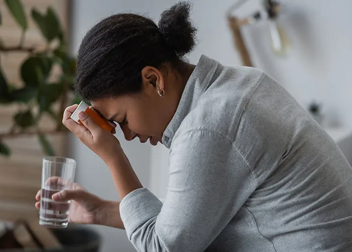 Woman feeling paranoid and distressed holding medication and glass of water in a home setting facing real-life terror situation.
