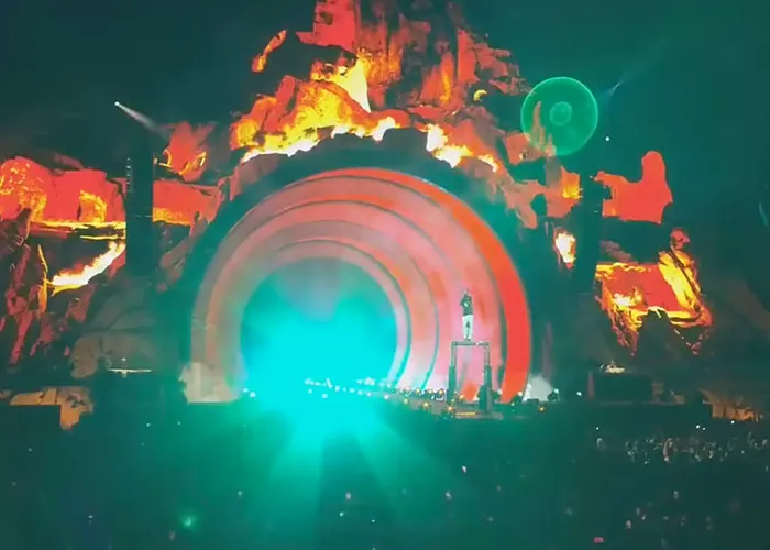 Concert stage with bright lights and glowing arches, capturing intense moment reflecting real-life terror and paranoia themes.