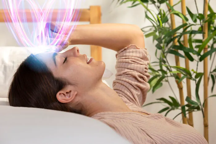 Young woman lying down with eyes closed, experiencing a glowing light effect symbolizing great unsolved mysteries.