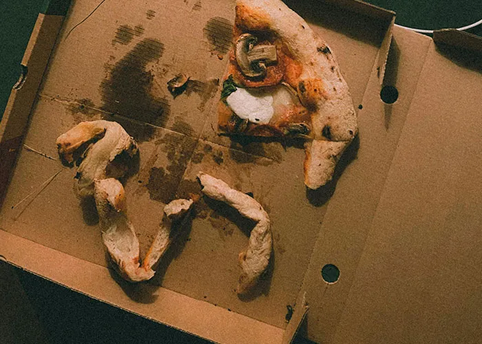 Partially eaten pizza in a greasy cardboard box, showing a funny fail with the crust shaped like numbers inside the box.