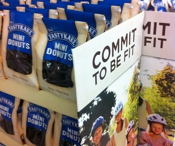 Packages of mini donuts displayed next to a fitness sign reading commit to be fit, an advertising placement fail.