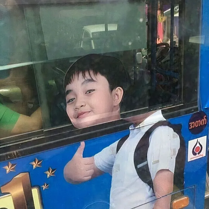 Boy giving thumbs up on a bus advertisement, blending awkwardly with the reflection for an advertising placement fail.