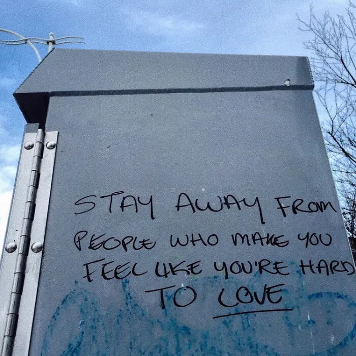 Graffiti message on a metal public utility box advising to stay away from people who make you feel hard to love.