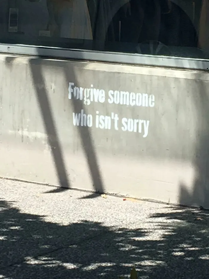 Vandalized public property with stencil graffiti saying Forgive someone who isn't sorry on a concrete wall outside.