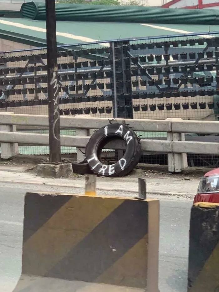 Tire with graffiti saying I am tired leaned against a fence, a creative example of people vandalizing public property.