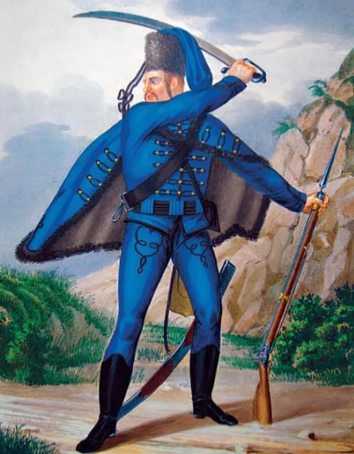 Man in an elaborate blue uniform holding a sword and rifle in a dramatic outdoor pose near rocky terrain and greenery.