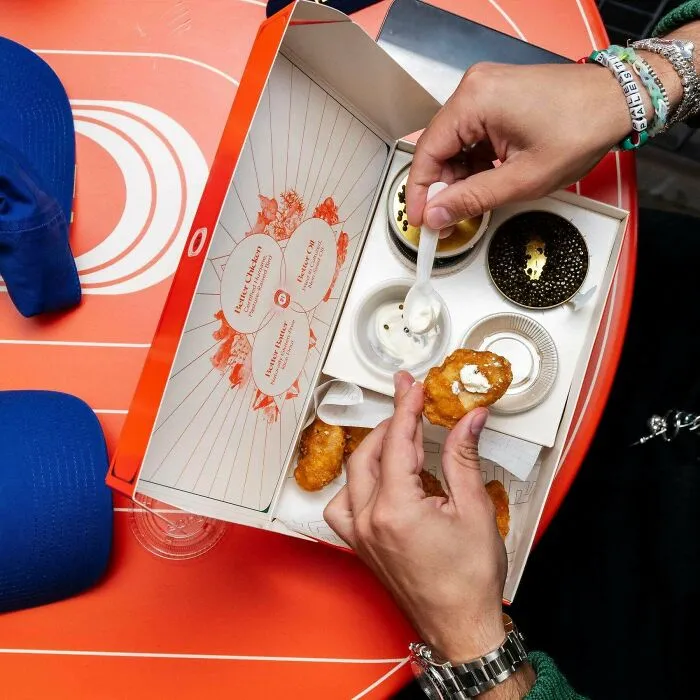 Hand dipping a fried dish into sauce from a gourmet box featuring unusual dishes from 102 dishes that are just stupid.