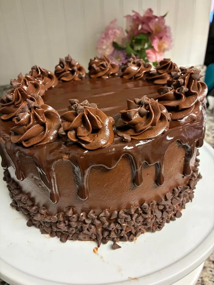 Chocolate cake with piped frosting, chocolate chips, and glossy ganache drip, showcasing gorgeous baked goods perfection.