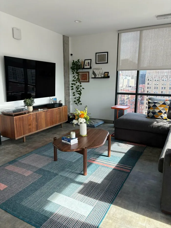 Modern living room with stylish home decor, wooden furniture, decorative plants, and large windows showcasing city views.