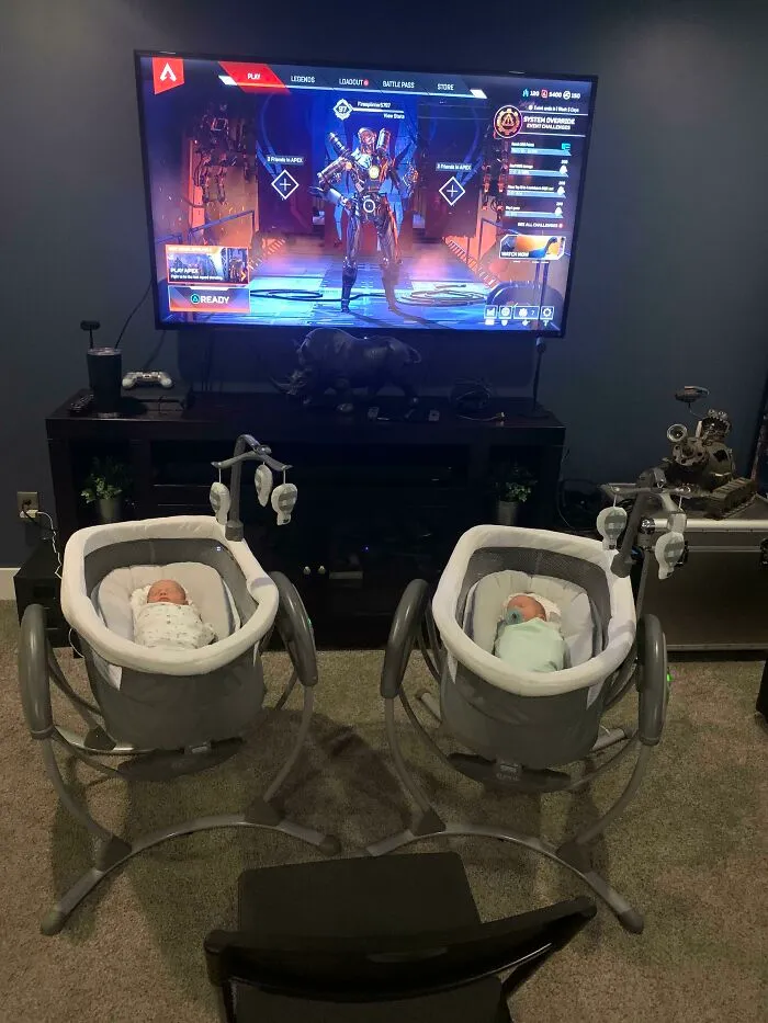Two babies in bassinets facing a television playing a video game, illustrating funny photos about differences between moms and dads.