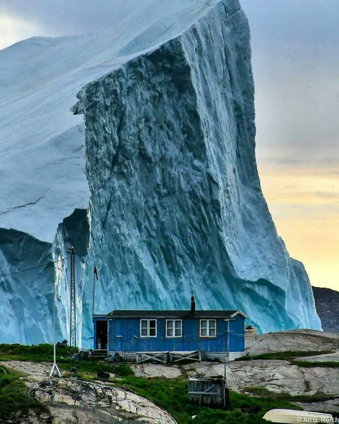 An Iceberg Passing Near A House In Greenland