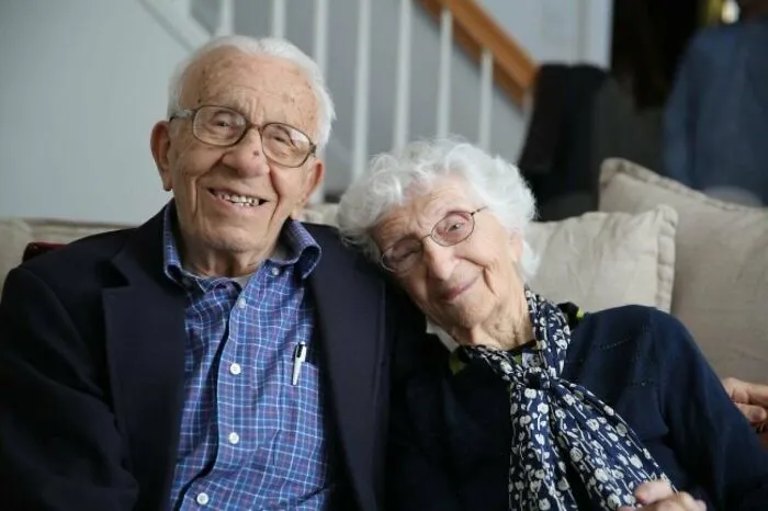Elderly couple smiling warmly on a couch, sharing a heartwarming moment in a cozy home setting.