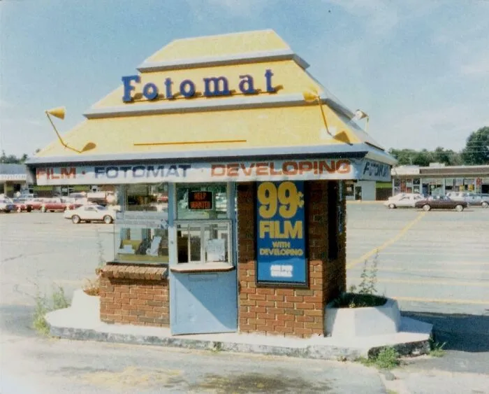 Vintage Fotomat film developing kiosk in a parking lot, evoking nostalgic memories and reminders of old age.