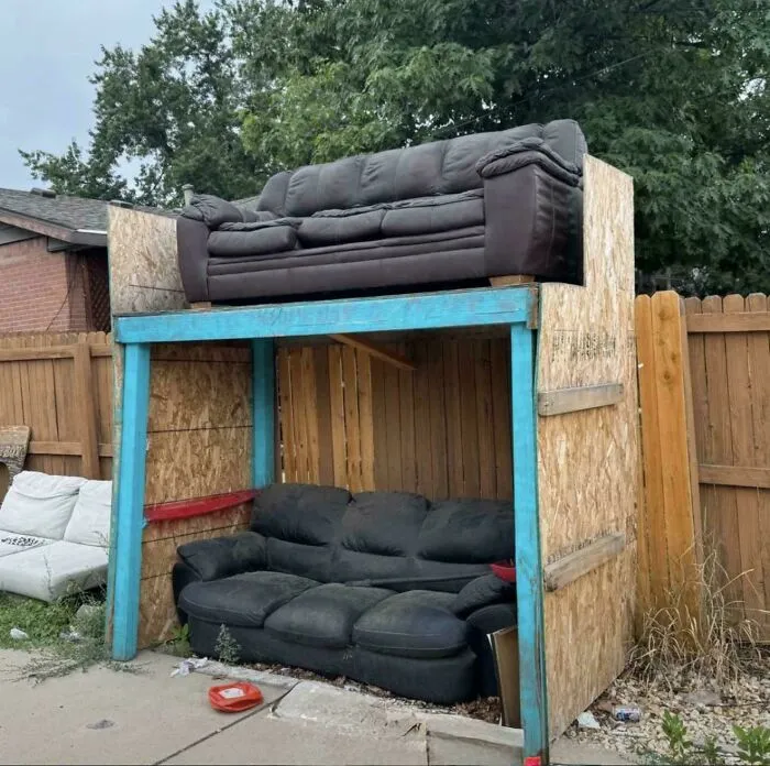Two sofas stacked vertically with a wooden frame enclosure demonstrating redneck engineer creativity outdoors.