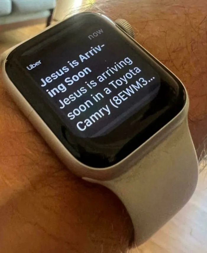 Smartwatch screen showing Uber notification stating Jesus is arriving soon in a Toyota Camry, combining holy and cursed humor.