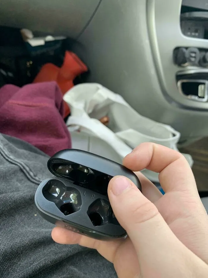 Auriculares inalámbricos vacíos en mano dentro de un coche, ejemplo de fotos de vacaciones que no salieron como se esperaba.