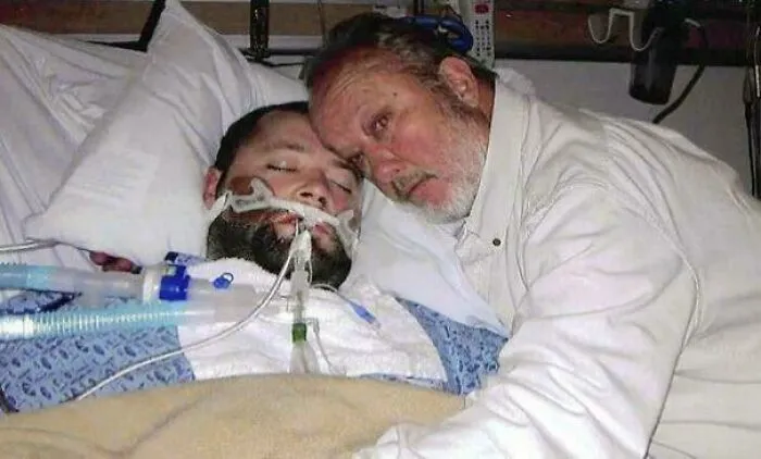 Man in hospital bed with breathing tube being comforted by an older man, highlighting facts still remain undiscovered.