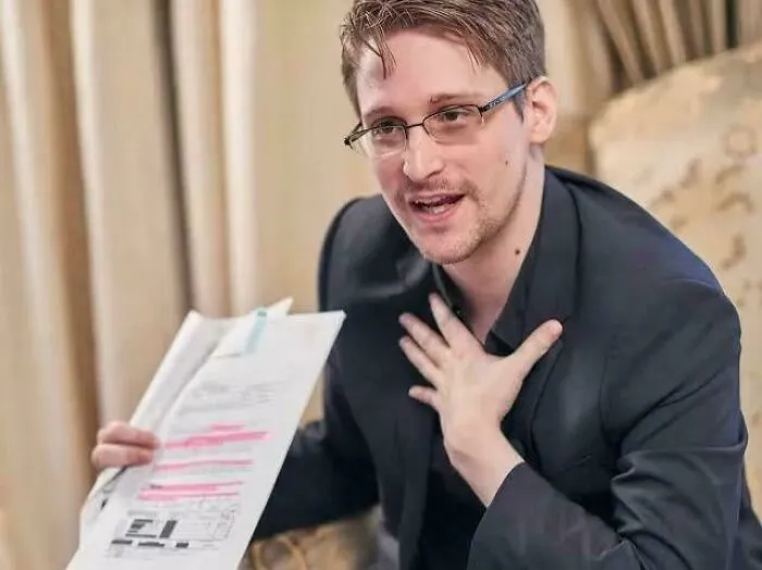 A man wearing glasses explains fascinating facts while holding highlighted documents in an indoor setting.