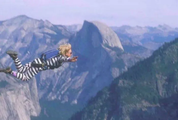 Person wearing striped outfit and backpack wingsuit flying over mountainous landscape, capturing fascinating facts still undiscovered.