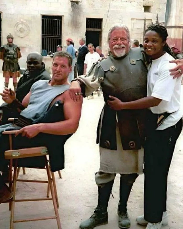 Actors in medieval costumes and casual attire posing on set, capturing a fascinating moment still remains undiscovered today.