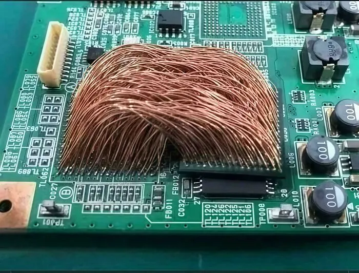 Close-up of a circuit board with tangled copper wires improperly soldered, illustrating common electronics handling mistakes.