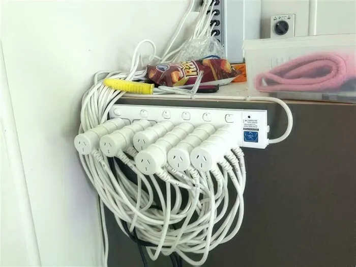 Overloaded power strip with many plugs and tangled cords creating a hazardous electronic handling situation.